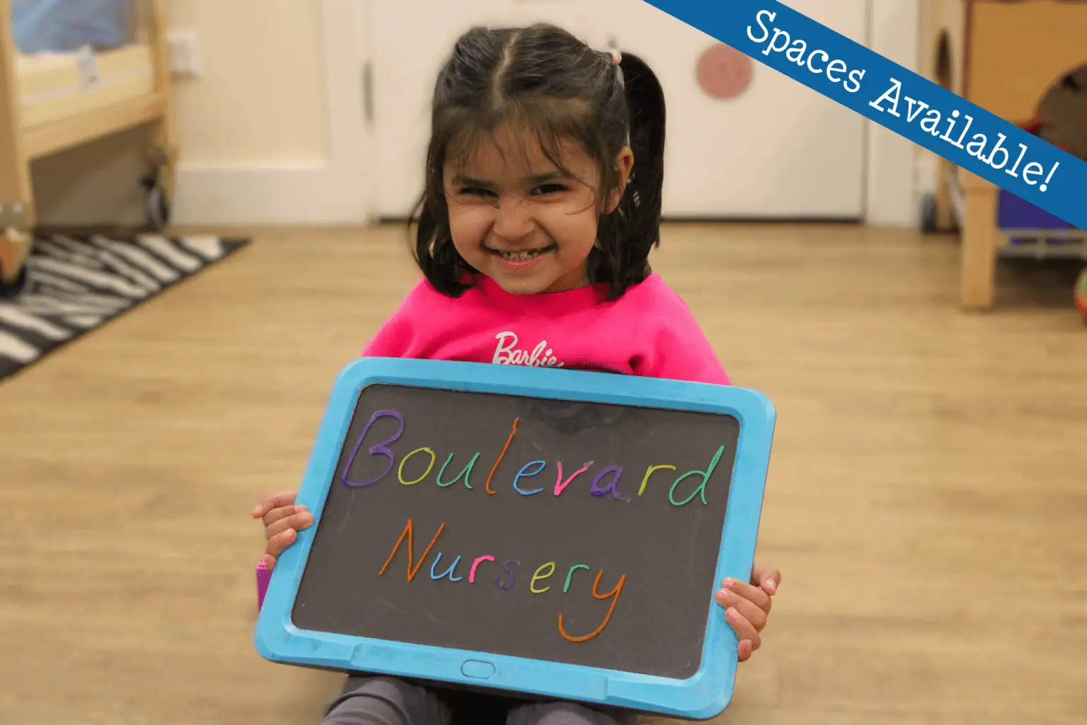 Girl holding sign saying Boulevard Nursery in multi-coloured handwritten text